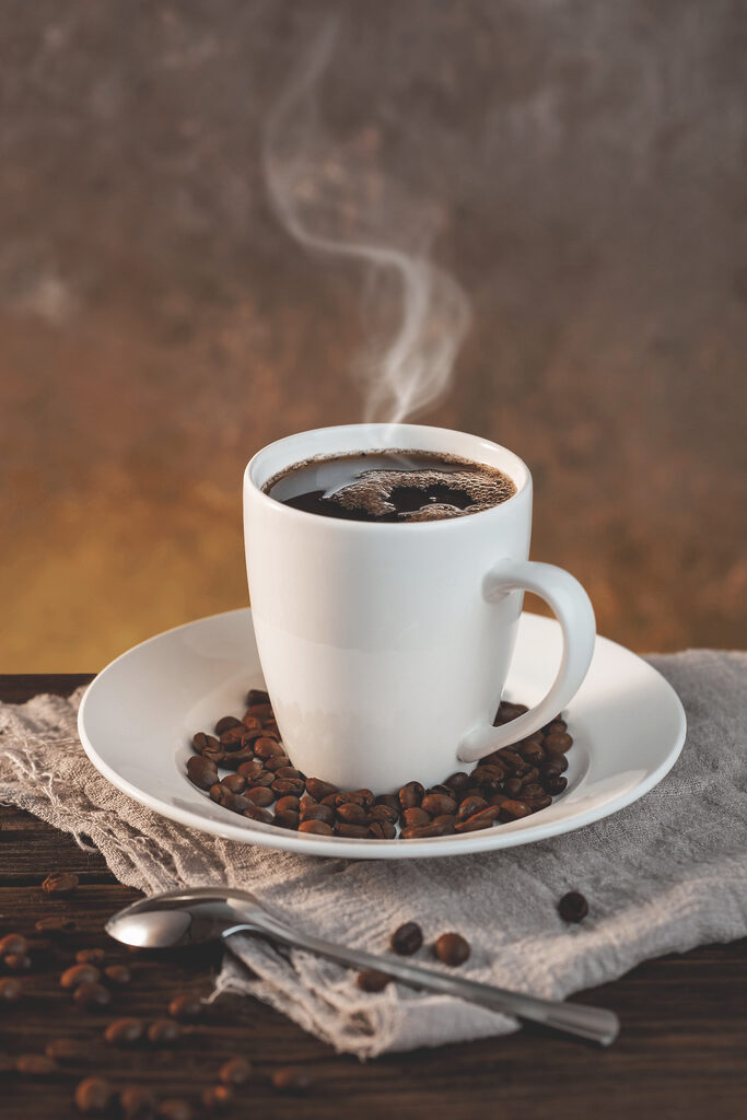 A cup of coffee on a plate with beans and a spoon